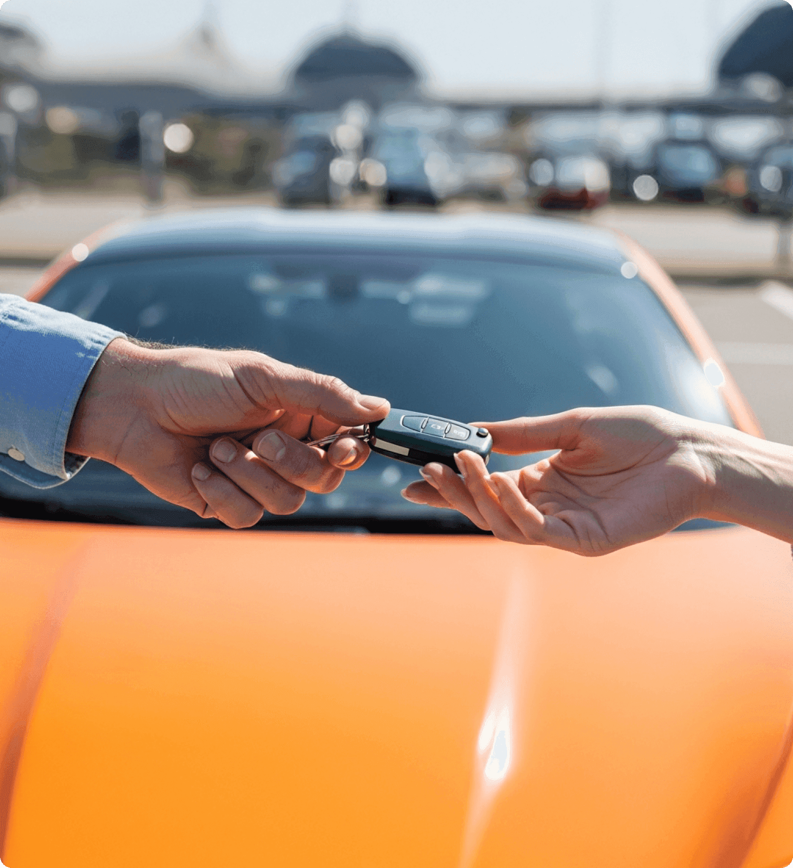 Close-up of hands exchanging car keys in front of a parked vehicle.