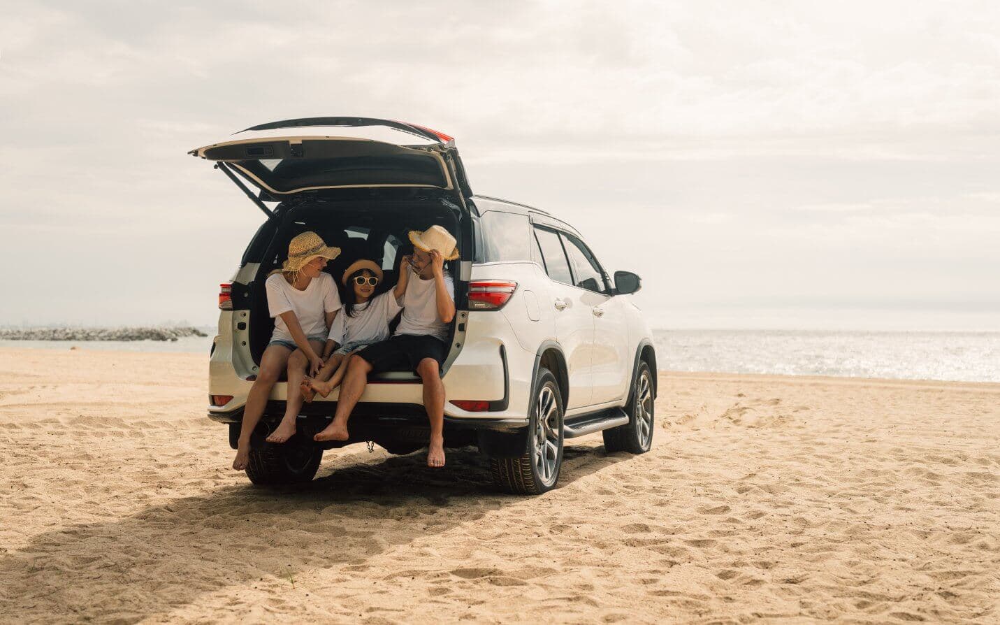 A family at the beach sitting together in the back of their vehicle